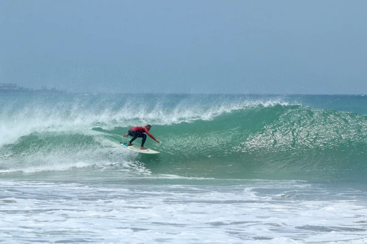 Surfista descendo a onda com a plataforma de petróleo ao fundo